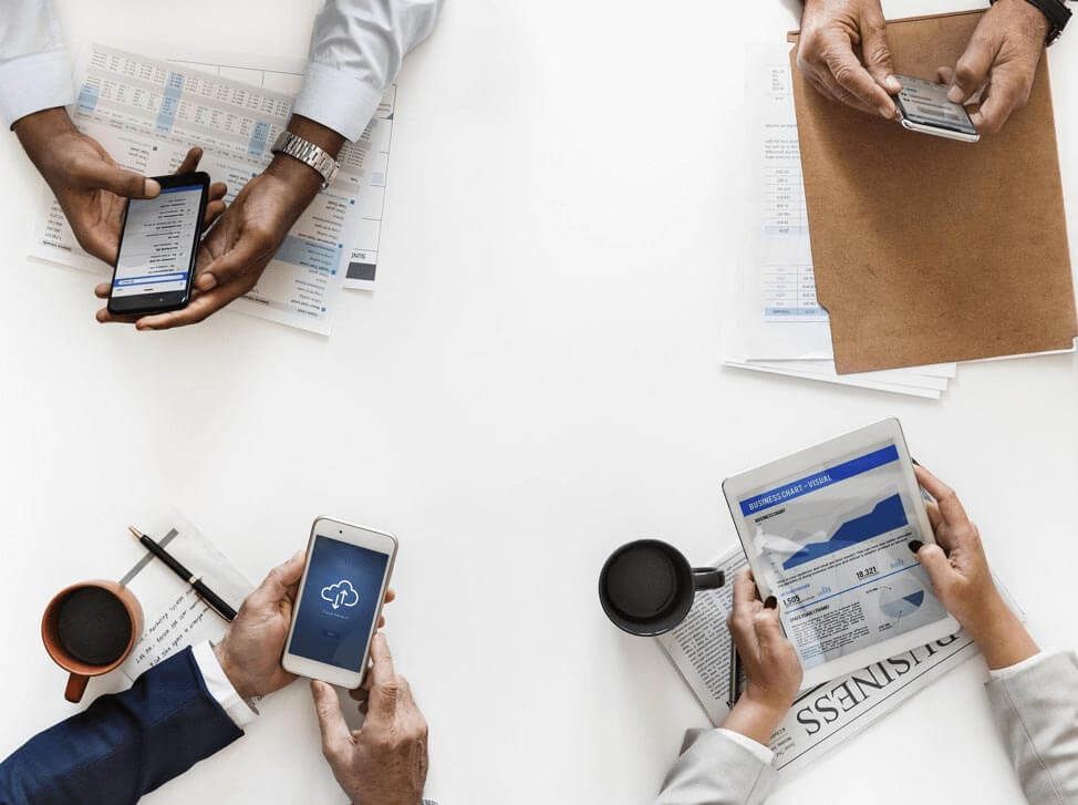 A group of men at a desk on their cellphones and newspaper